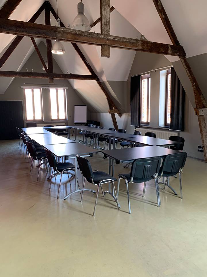 Zaal met 12 tafels en whiteboard onder de nok van het dak