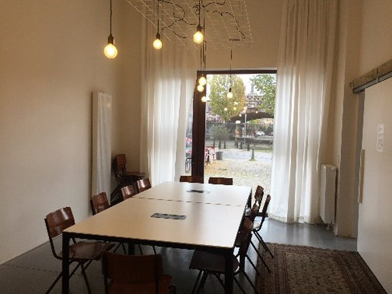 Kleine zaal met 11 stoelen rond een centrale tafel op het gelijkvloers uitkijkend op de Draakplaats